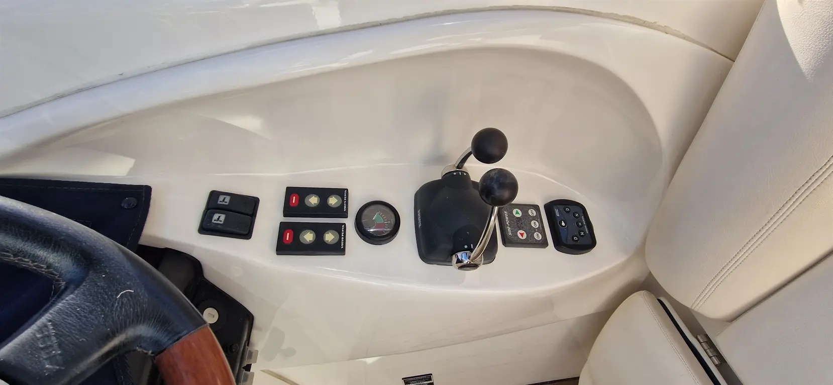 Boat control panel featuring throttle, buttons for navigation, and a gauge, with a leather steering wheel visible.